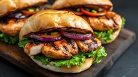 Grilled chicken burgers with fresh lettuce and red onion on wooden board. Juicy barbecue sandwiches ready to serve for lunch or dinner meal preparation.