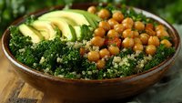 Nutritious vegan bowl with roasted chickpeas, fresh avocado slices, and kale quinoa mix served in rustic ceramic bowl on wooden surface.