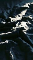 Crumpled dark blue fabric with dramatic sunlight casting sharp shadows across textured folds, creating contrast and depth for design and textile projects.