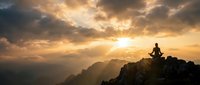 Person meditating on mountain peak at golden sunset with dramatic clouds and scenic valley view below for wellness and mindfulness concepts.