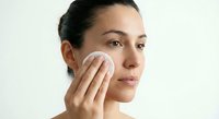 Young woman applying skincare product with cotton pad on face during daily beauty routine for healthy glowing skin and facial care regimen.