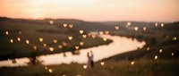 Romantic heart-shaped bokeh lights over serene river landscape at golden hour sunset creating dreamy atmosphere for wedding photography and love concepts.
