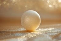 Translucent golden sphere resting on sparkling sand with warm bokeh background, suitable for abstract design, wellness, and luxury branding projects.