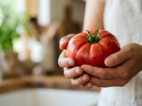 Farmer holding fresh ripe red tomato with green stem in hands at home kitchen. Organic produce, harvest, and healthy eating concept for culinary and agricultural use.