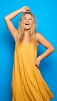 Happy young blonde woman in yellow dress laughing with hand in hair against bright blue background for lifestyle and fashion content.