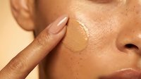 Young woman applying liquid foundation makeup to face with finger showing skincare routine and cosmetic application process for beauty and personal care.