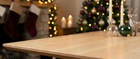 Empty wooden table surface with blurred Christmas decorations, stockings, tree lights and candles in cozy holiday home interior background for product display.