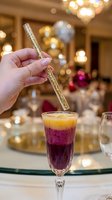Woman holding decorative straw in layered cocktail at elegant dinner event with warm ambient lighting and festive table setting for entertaining and celebration.