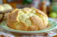 Freshly baked crusty bread with soft yellow interior on green plate, cracked golden-brown top showing fluffy texture inside, homestyle artisanal loaf on checkered cloth.