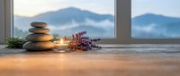 Zen spa stones balanced on wooden windowsill with lavender flowers and candle, mountain view background for wellness meditation relaxation therapy.