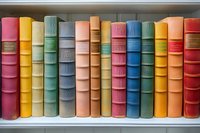 Row of vintage hardcover books in various pastel and bright colors arranged on white shelf, spines showing classic binding details and decorative elements.