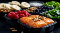 Fresh salmon fillet with berries, nuts and greens in meal prep containers on dark background. Healthy balanced lunch boxes with omega-3 rich protein.
