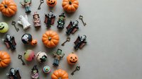Halloween flat lay with miniature pumpkins, spooky character figurines, vintage keys and festive decorations arranged on neutral background for autumn celebration.