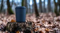 Dark blue disposable coffee cup on tree stump surrounded by fallen autumn leaves in moody forest setting, shallow depth of field creates atmospheric outdoor scene.