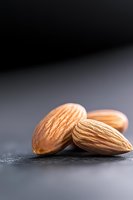 Fresh whole almonds on dark stone background with dramatic lighting and selective focus, macro food photography for healthy eating concept.