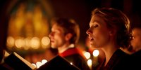 Young woman singing in choir during church service, illuminated by warm candlelight, creating spiritual atmosphere for religious ceremony.