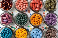 Colorful pharmaceutical pills and capsules in glass jars viewed from above. Various medications in different shapes, sizes and colors arranged in neat rows.