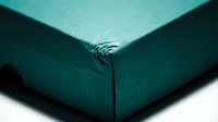 Teal fitted bed sheet with elastic corners on white background, isolated textile bedding for interior design and home decor projects.