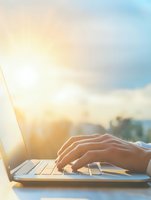 Female hands typing on laptop keyboard at sunset with soft golden light and bokeh background, remote work concept for business and freelance lifestyle.