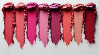 Crushed and smeared lipstick or eyeshadow swatches in various shades of pink, coral and burgundy showing texture and pigmentation on white background.