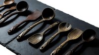 Handcrafted wooden spoons collection with natural wood grain patterns arranged on dark slate surface for rustic kitchen and cooking themes.