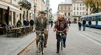 Senior couple cycling together through historic European city center with autumn leaves and vintage bicycles enjoying active retirement lifestyle.