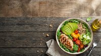 Grilled salmon fillet with quinoa, avocado, tomato and cucumber in green bowl on wooden table, healthy lunch meal for diet and nutrition.