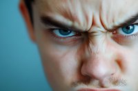 Close-up portrait of angry young Caucasian man with intense blue eyes and furrowed brow expressing frustration and rage against turquoise background.