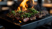 Juicy grilled steak with fresh herbs and seasonings seared to perfection on black cast iron pan with dramatic flames and smoke, close up view of medium rare beef.
