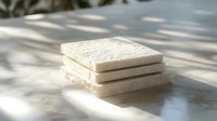 Stack of white marble stone coasters on light surface with natural shadow pattern overlay, minimalist home decor composition in soft morning light.