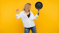 Blonde woman in white shirt holding frying pan on vibrant yellow background, cooking concept for kitchen advertising and culinary content.