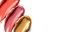 Colorful lipstick smears in coral pink and gold tones on white background. Cosmetic texture swatches for beauty and makeup design projects.
