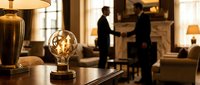 Vintage Edison bulb glowing on luxury hotel reception desk with two businessmen shaking hands in blurred background, warm ambient lighting for corporate hospitality concepts.
