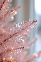 Pink artificial Christmas tree branches with soft glowing lights and delicate ornaments create dreamy holiday atmosphere, close-up macro view in pastel tones.