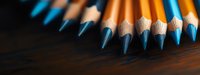 Sharp blue pencils arranged in row on dark wooden surface with dramatic lighting and shallow depth of field, creative stationery composition for education and art.