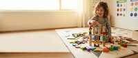 Young girl playing with colorful wooden building blocks on floor in bright playroom. Child development and educational toys for creative learning.