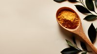 Wooden spoon filled with vibrant curry powder and spices on neutral beige background with fresh green leaves, minimalist food photography composition.