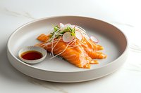 Fresh salmon sashimi slices garnished with daikon radish sprouts and pink radish on gray ceramic plate, served with soy sauce dipping bowl on marble surface.