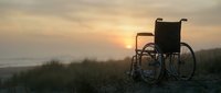 Empty wheelchair silhouetted against golden sunset over misty coastal landscape, symbolizing hope, accessibility, and overcoming challenges in healthcare and rehabilitation contexts.