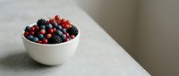 Mixed berries including blackberries, red currants, and blueberries in a white ceramic bowl on a light surface for food and nutrition content.