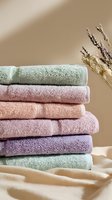 Stack of soft pastel colored bath towels with dried lavender sprigs against neutral beige background, perfect for spa, bathroom decor, or home textiles.
