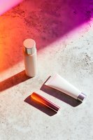 Minimalist cosmetic products on textured surface with vibrant orange and purple light casting dramatic shadows, modern beauty composition for skincare advertising.