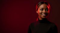 Young African American woman smiling confidently in black turtleneck against red background with dramatic lighting for professional headshot photography.