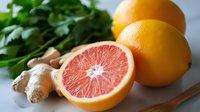 Fresh pink grapefruit cut in half with whole citrus fruits, ginger root and green herbs on light background, healthy food ingredients for cooking.