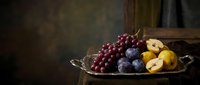 Elegant fruit arrangement with red grapes, plums and yellow apples in vintage metal tray on rustic wooden surface with dramatic lighting for culinary content.