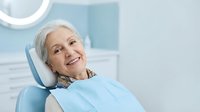 Senior Caucasian woman smiling confidently in dental chair wearing protective bib during routine checkup at modern clinic for oral health care.