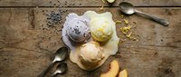 Homemade ice cream scoops in pastel colors on rustic wooden surface with vintage spoons and scattered toppings for dessert and culinary content.