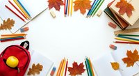 Autumn creative workspace with colorful pencils, books, red mug and orange maple leaves arranged in circle on white background for seasonal art projects.
