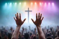 Raised hands in worship against glowing cross and colorful stage lights, silhouetted crowd of people at religious concert or church service gathering.
