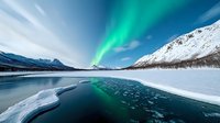 Spectacular aurora borealis dancing over frozen mountain lake with cracked ice surface reflecting green northern lights against snowy peaks in winter landscape.